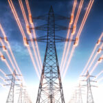 High voltage transmission towers with red glowing wires against blue sky. (Getty Images)