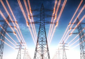 High voltage transmission towers with red glowing wires against blue sky. (Getty Images)